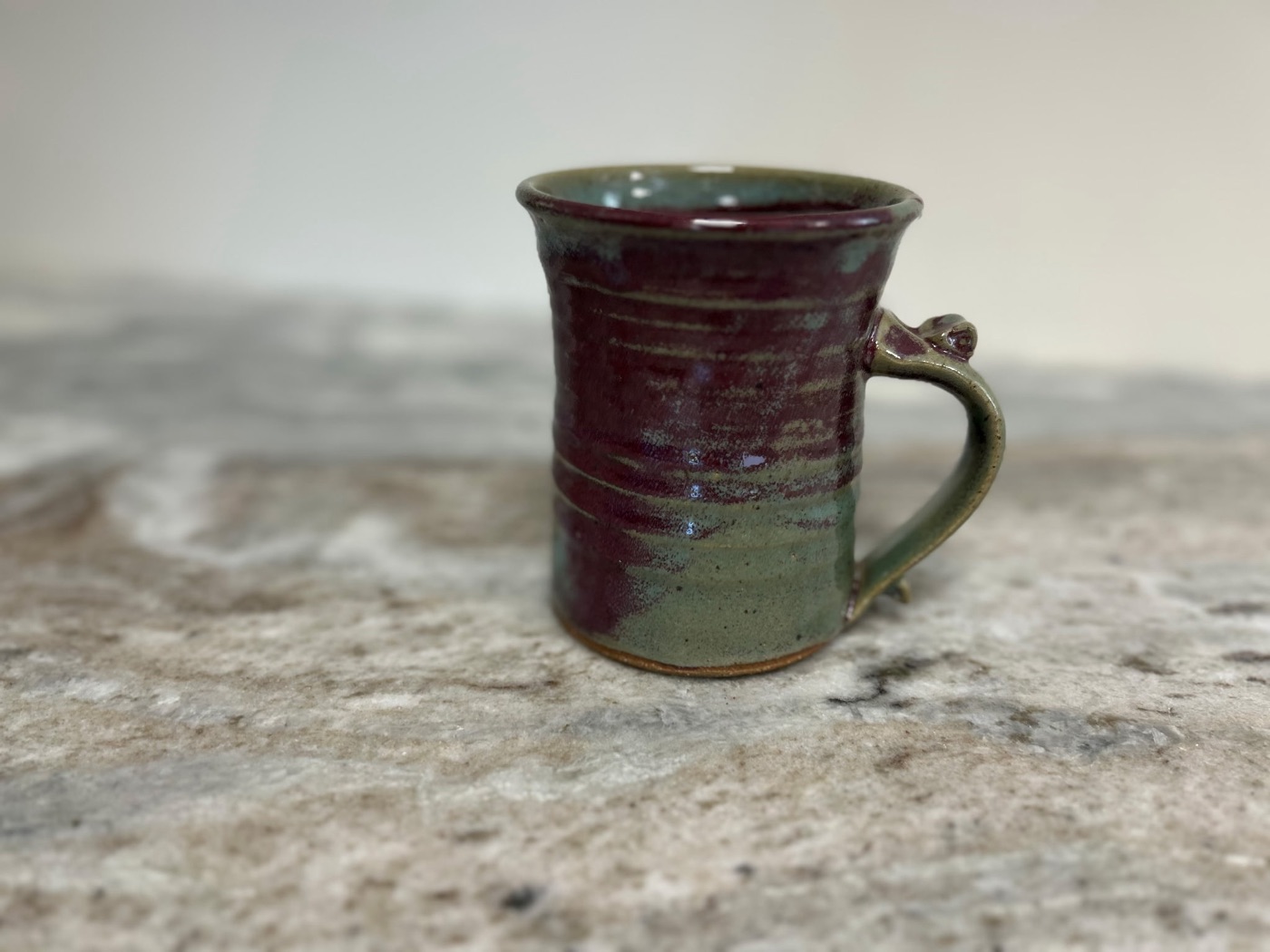 Handmade stoneware mug glazed burgundy on top and sage green below, with flared rim