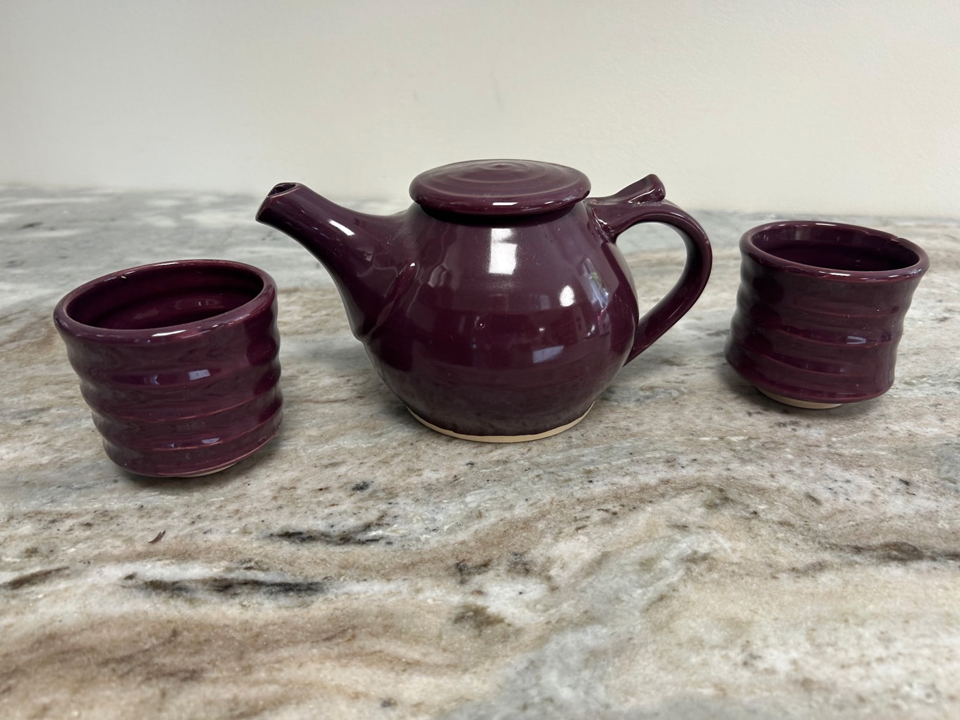 Handmade glossy burgundy pottery teapot with two matching ribbed cups