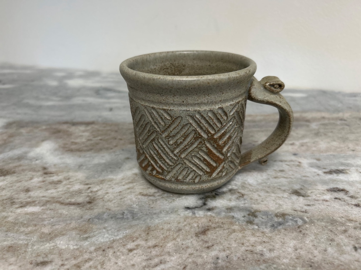 Handmade speckled cream pottery cup with hand-carved basketweave pattern
