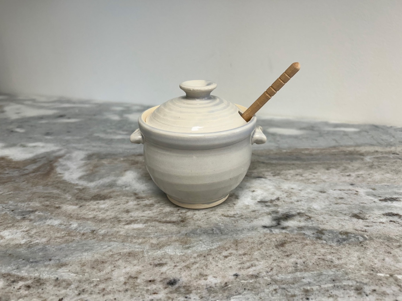 Handmade cream and white striped pottery honey pot with lid, small handles, and wooden honey dipper