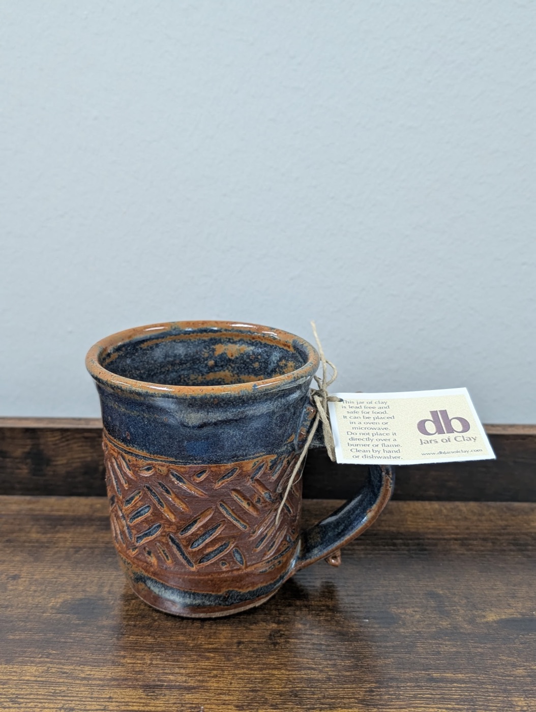 Handmade stoneware mug with indigo rim, rust body, and carved diamond pattern