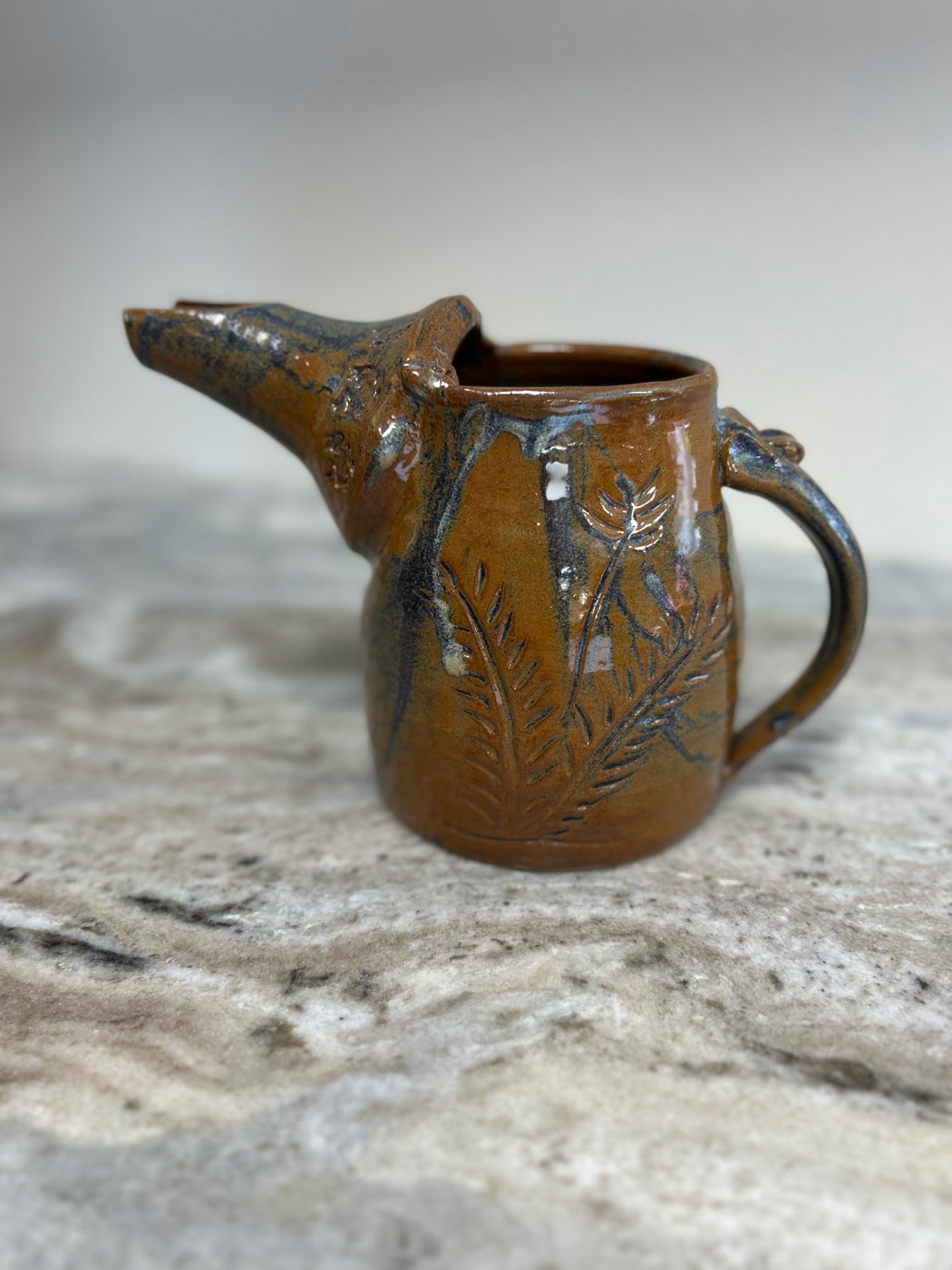 Handmade large rust-glazed pottery pitcher with carved fern motifs and sculpted spout