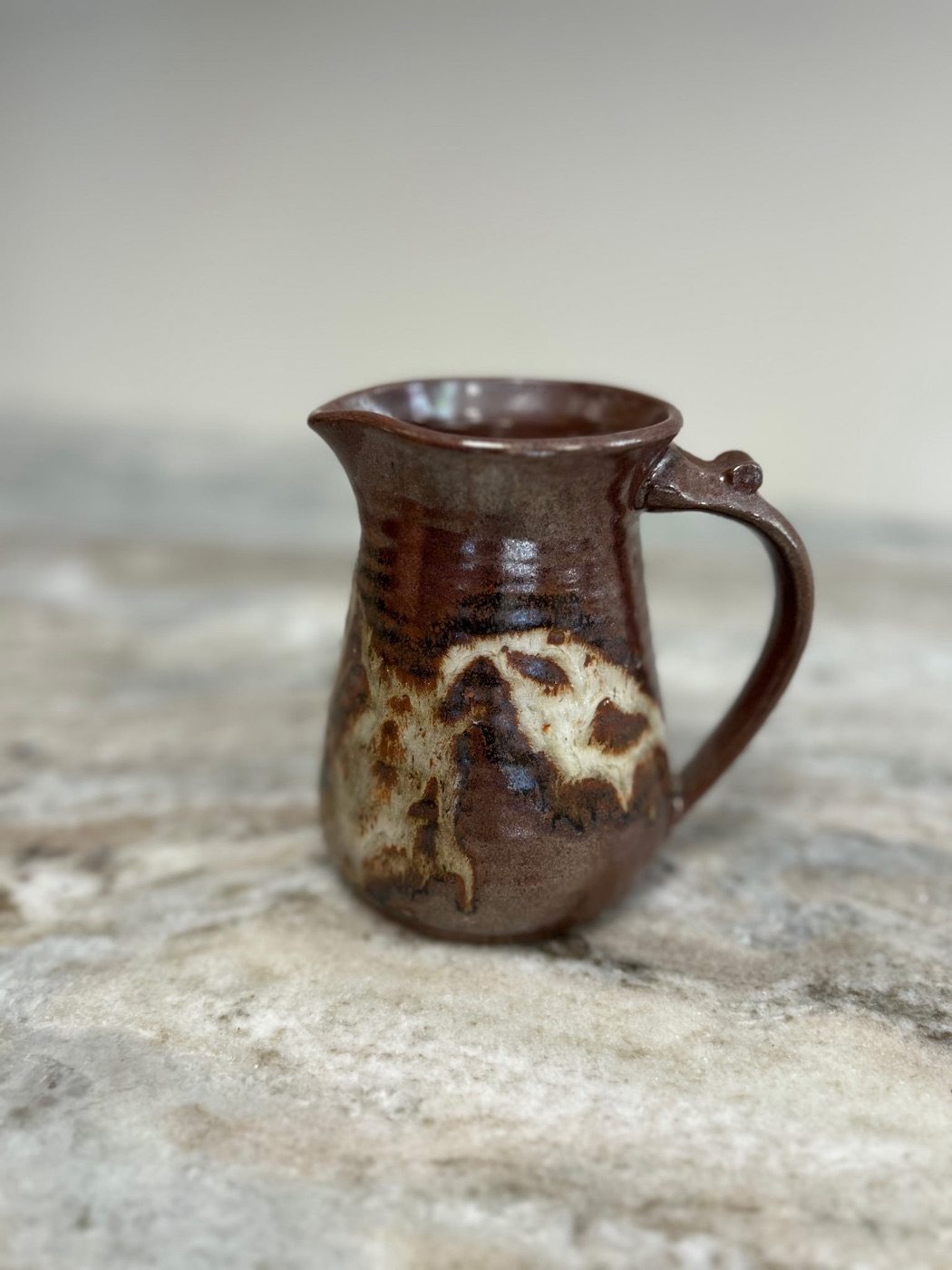 Handmade pottery pitcher in deep rust glaze with cream drip pattern and sculpted handle