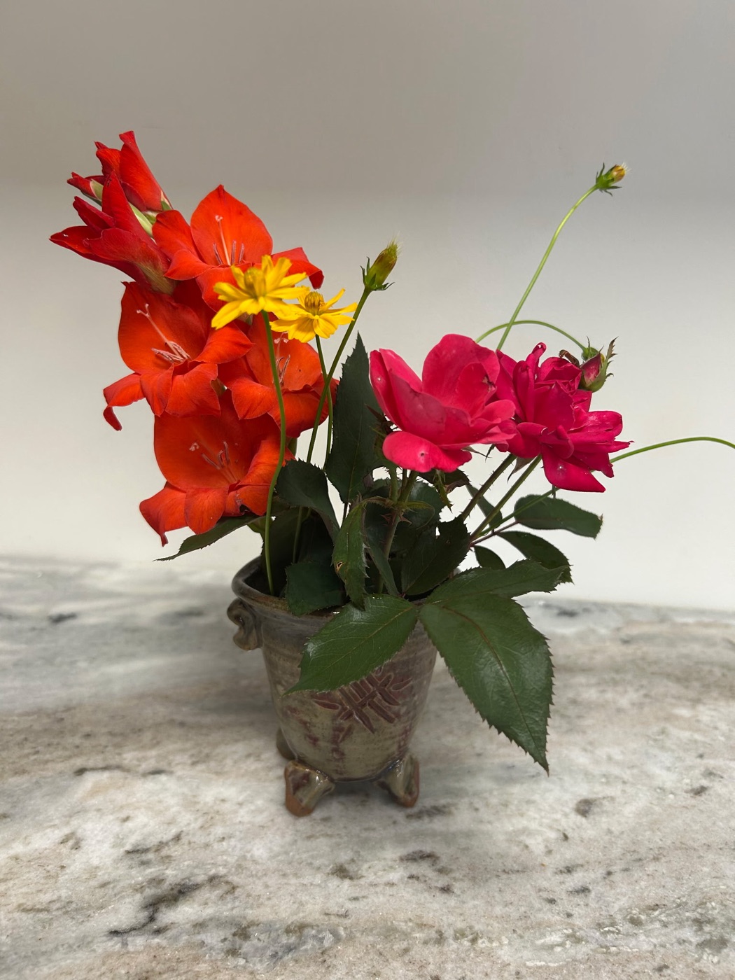 Handmade rust-glazed stem bowl with carved leaf pattern and three feet, shown holding cut flowers