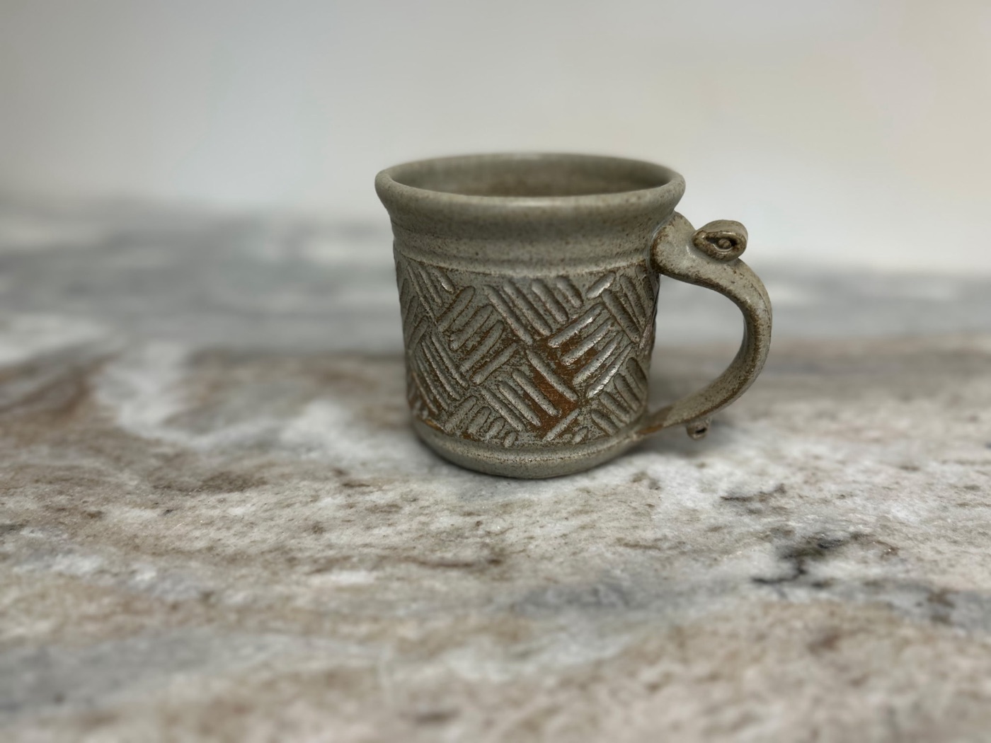 Handmade pottery cup with warm speckled cream glaze and hand-carved basketweave